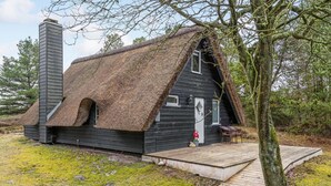 A thatched-roof cabin with a wooden deck, a chimney, and a door with a window. - Lovely home in Rømø with kitchen (Rømø)
