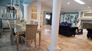 A spacious living room with a large white column, a dining area with a wooden table and chairs, and a kitchen in the background. -  Luxury Estate with Dual Pools on 2.5 Acres Near Downtown Sarasota & Beaches (Sarasota)