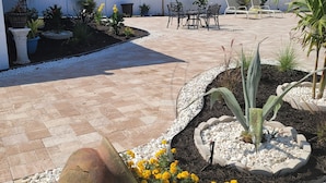 A patio area with outdoor seating, a decorative stone, and a variety of plants. -  Luxury Estate with Dual Pools on 2.5 Acres Near Downtown Sarasota & Beaches (Sarasota)