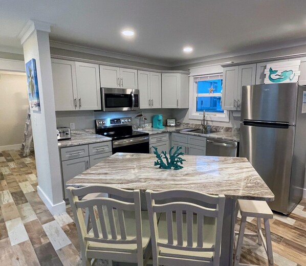 A modern kitchen with white cabinets, stainless steel appliances, a marble island, and a checkered floor.