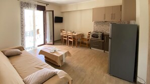 Een kamer met een bed, een eettafel met stoelen, een keuken met een magnetron en koelkast, en een aan de muur bevestigde televisie.