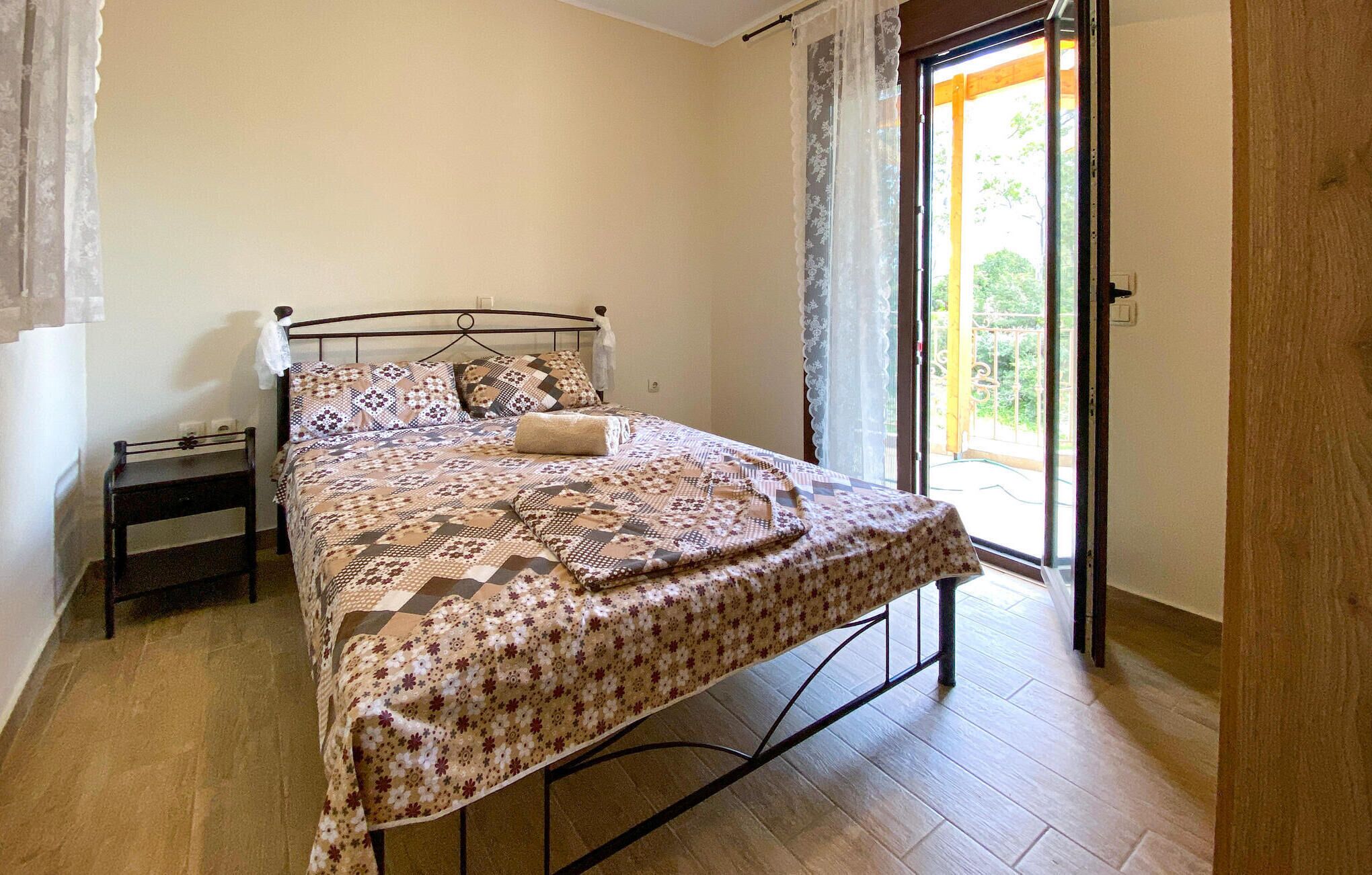 Een slaapkamer met een bed, een nachtkastje, een raam met gordijnen en uitzicht op de omgeving.