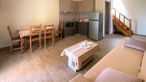 Een knus woongedeelte met een kitchenette, een eethoek met houten stoelen, een bank en een trap.