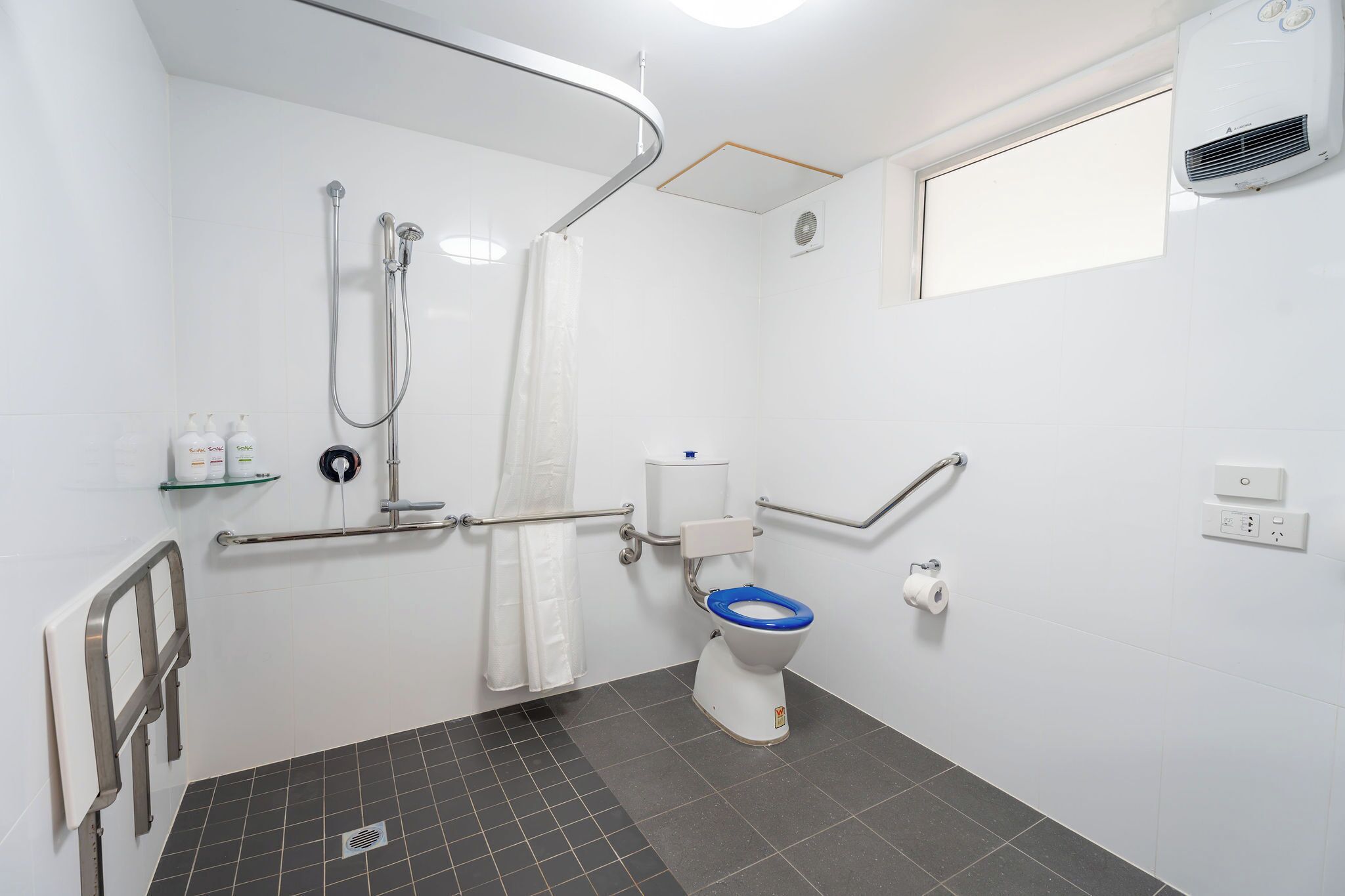 A bathroom with a shower, toilet, grab bars, and a window.
