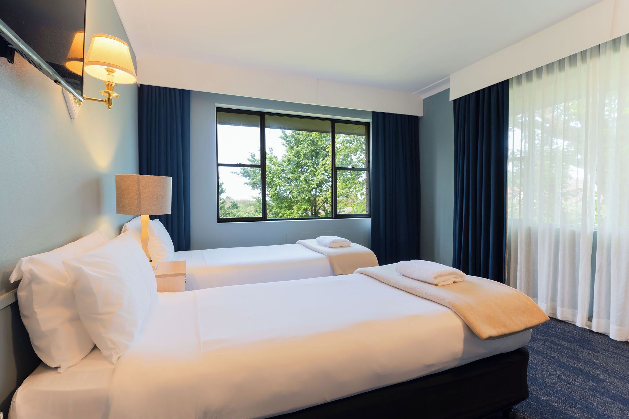 A hotel room with two beds, a large window, and a lamp.
