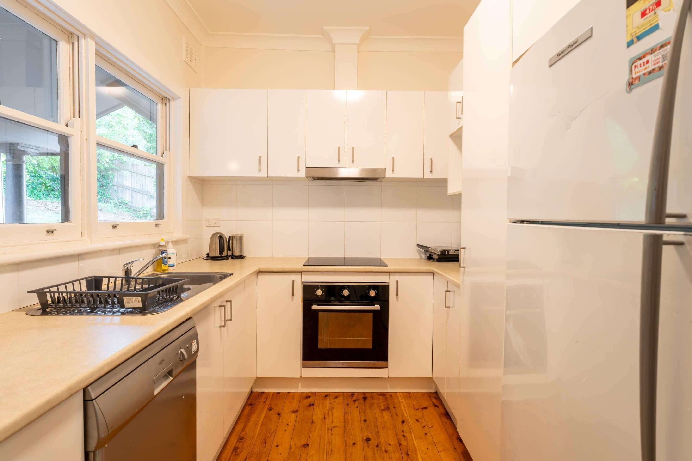 A compact kitchen with white cabinets, a stainless steel oven, a dishwasher, and a refrigerator.