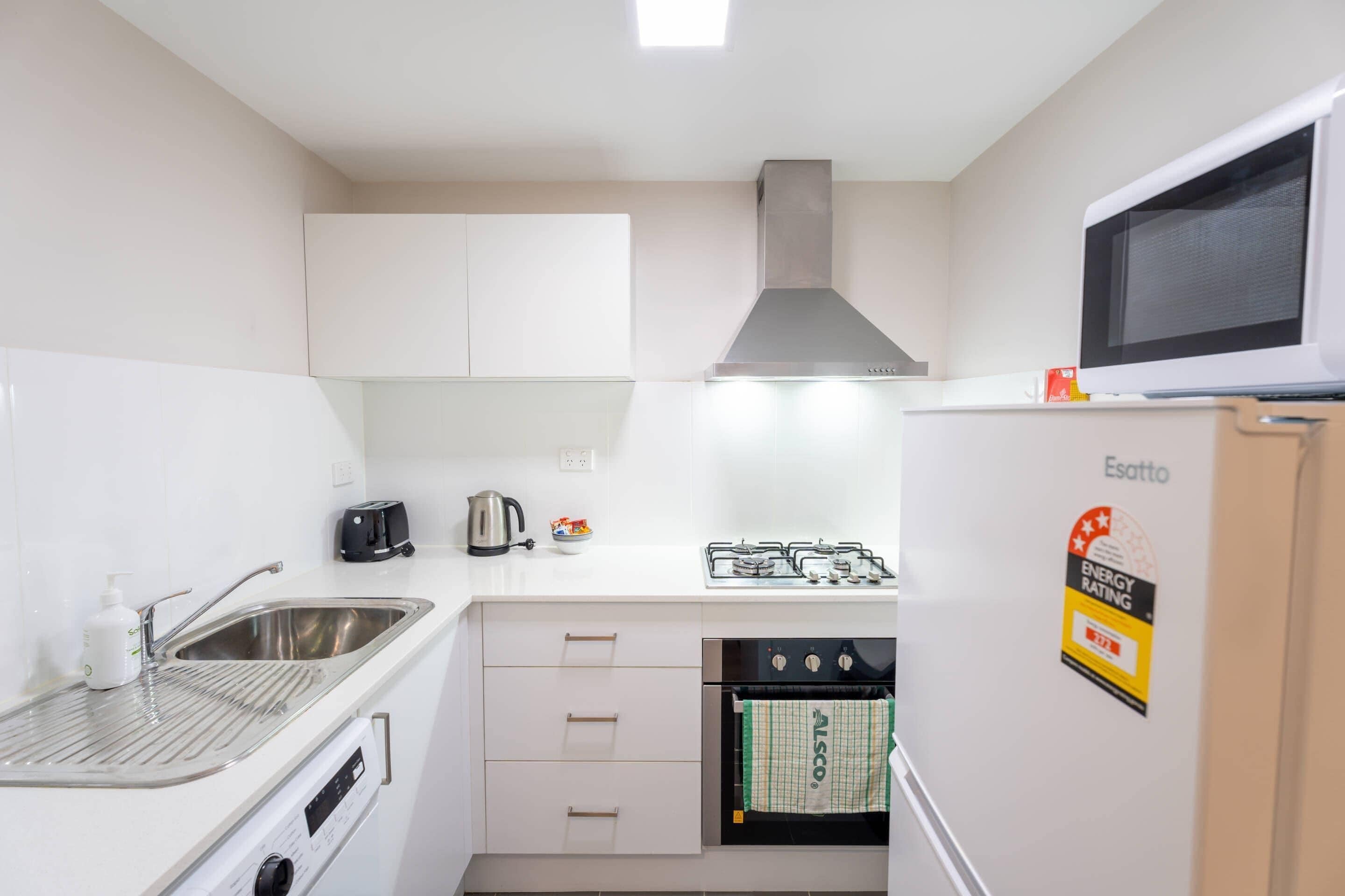 Una cocina compacta con armarios blancos, un lavamanos de acero inoxidable, una estufa a gas, un horno y un microondas.