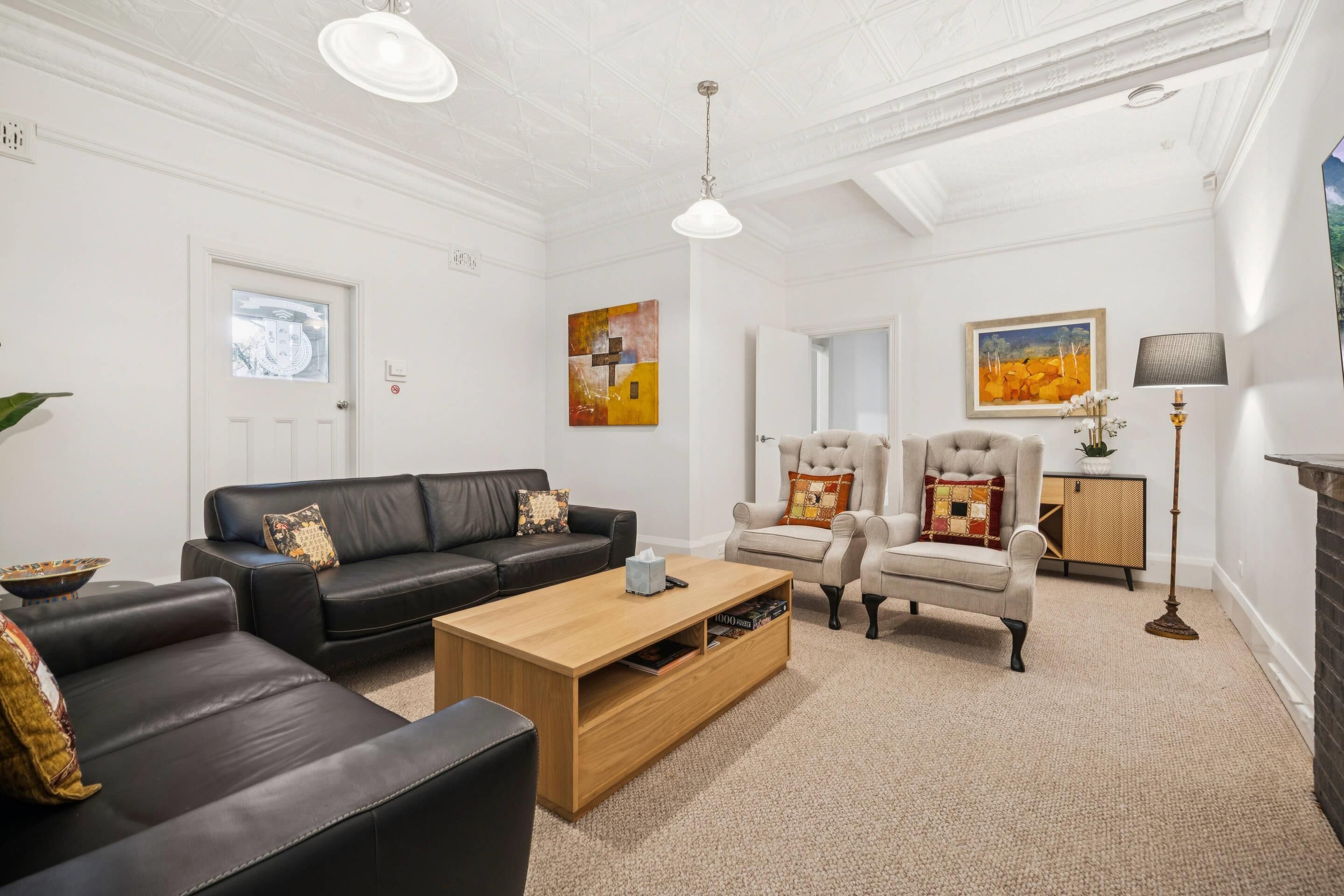 A living room with a black leather sofa, a wooden coffee table, a beige armchair, and a fireplace.