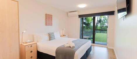 A modern bedroom with a bed, bedside tables, a TV, and a sliding glass door to a balcony.