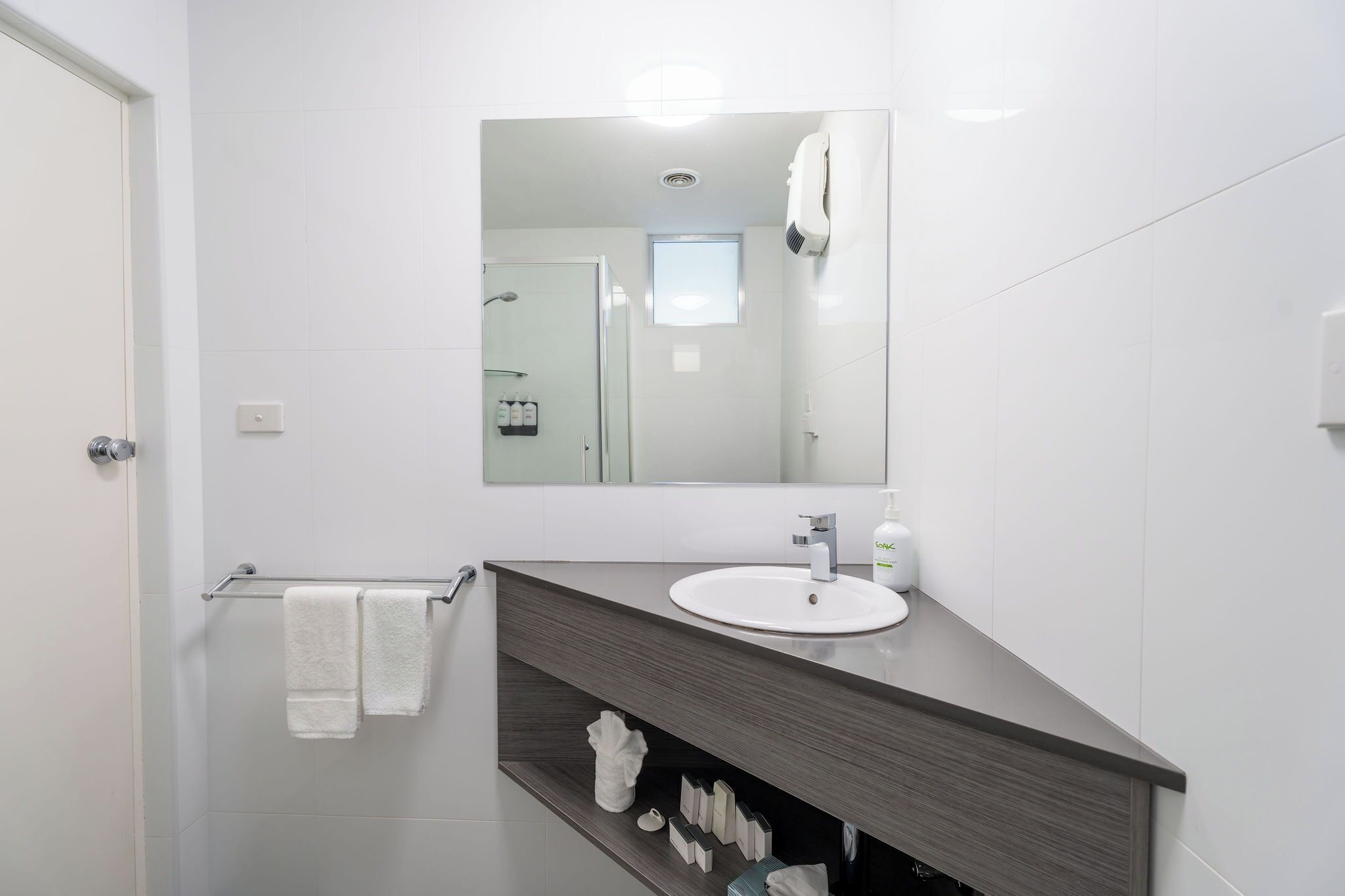 A modern bathroom with a white sink, dark countertop, and a large mirror.