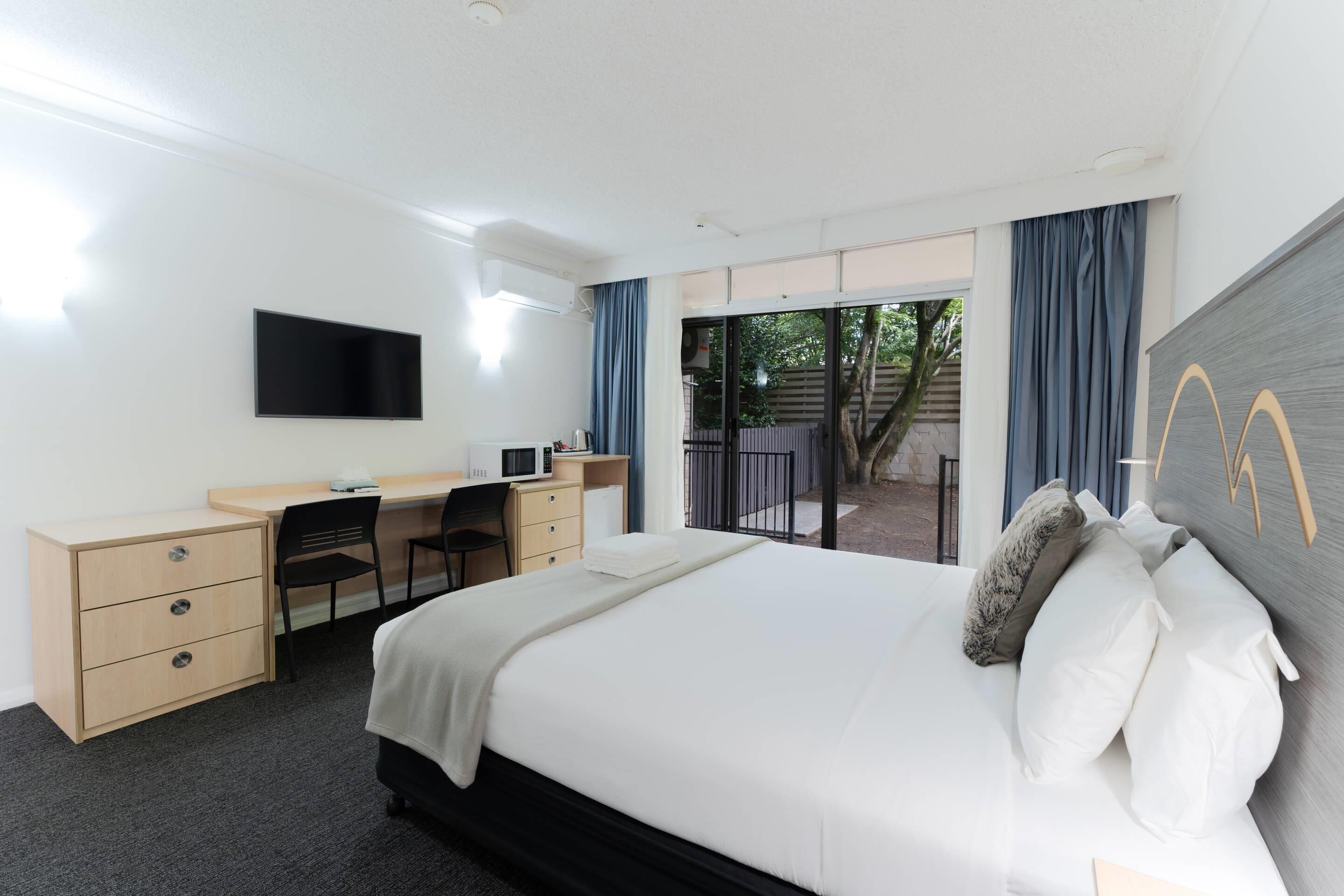Een hotelkamer met een bed, bureau, stoel, televisie en balkon met gordijnen.