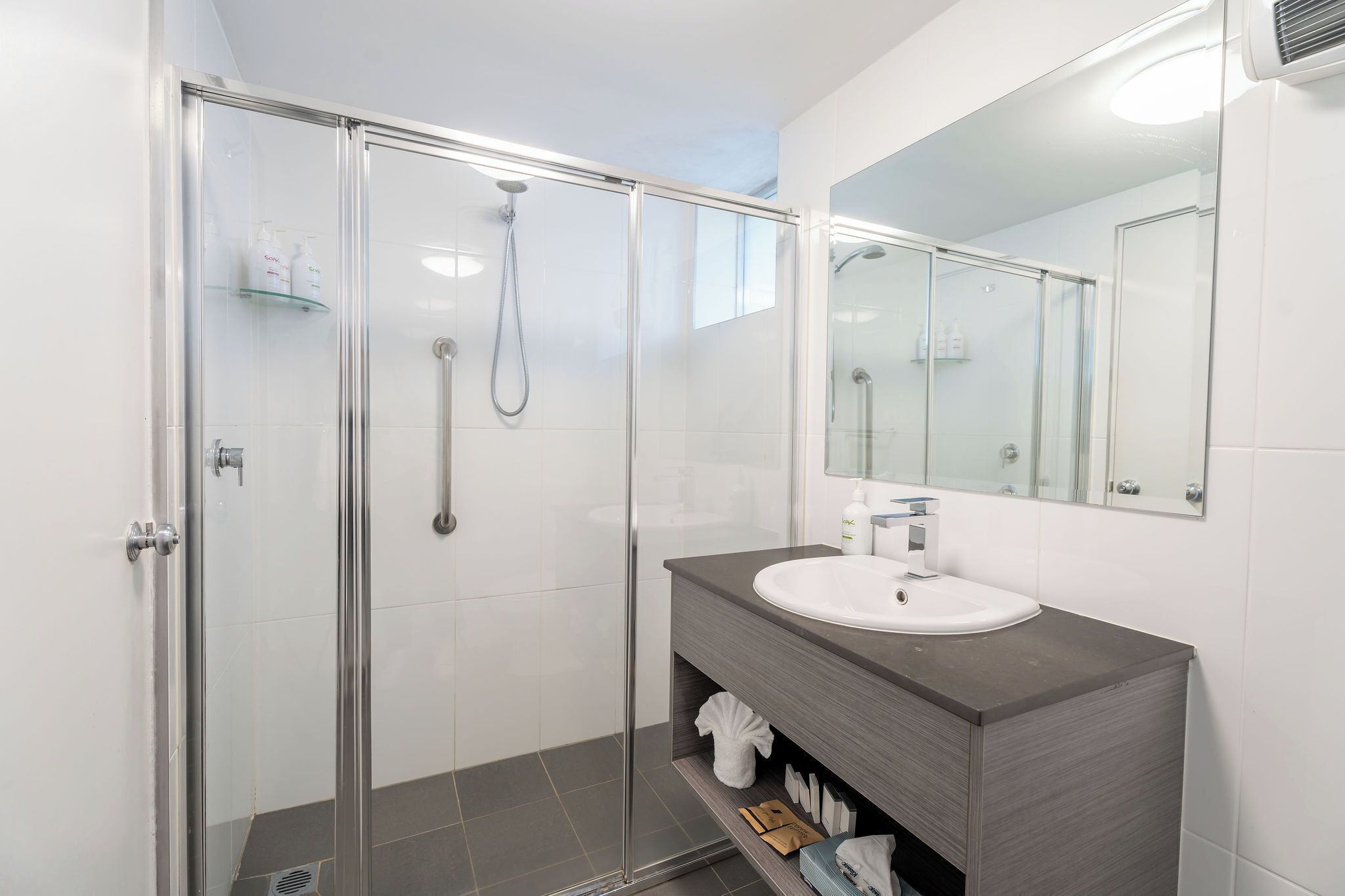 A modern bathroom with a glass-enclosed shower, a white sink, and a large mirror.