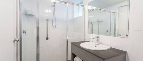 A modern bathroom with a glass-enclosed shower, a white sink, and a large mirror.