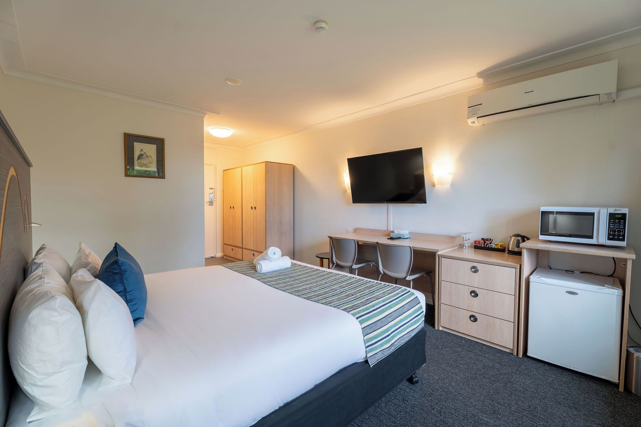 Habitación de hotel con cama, escritorio, televisión, microondas y refrigerador pequeño.