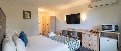 Habitación de hotel con cama, escritorio, televisión, microondas y refrigerador pequeño.