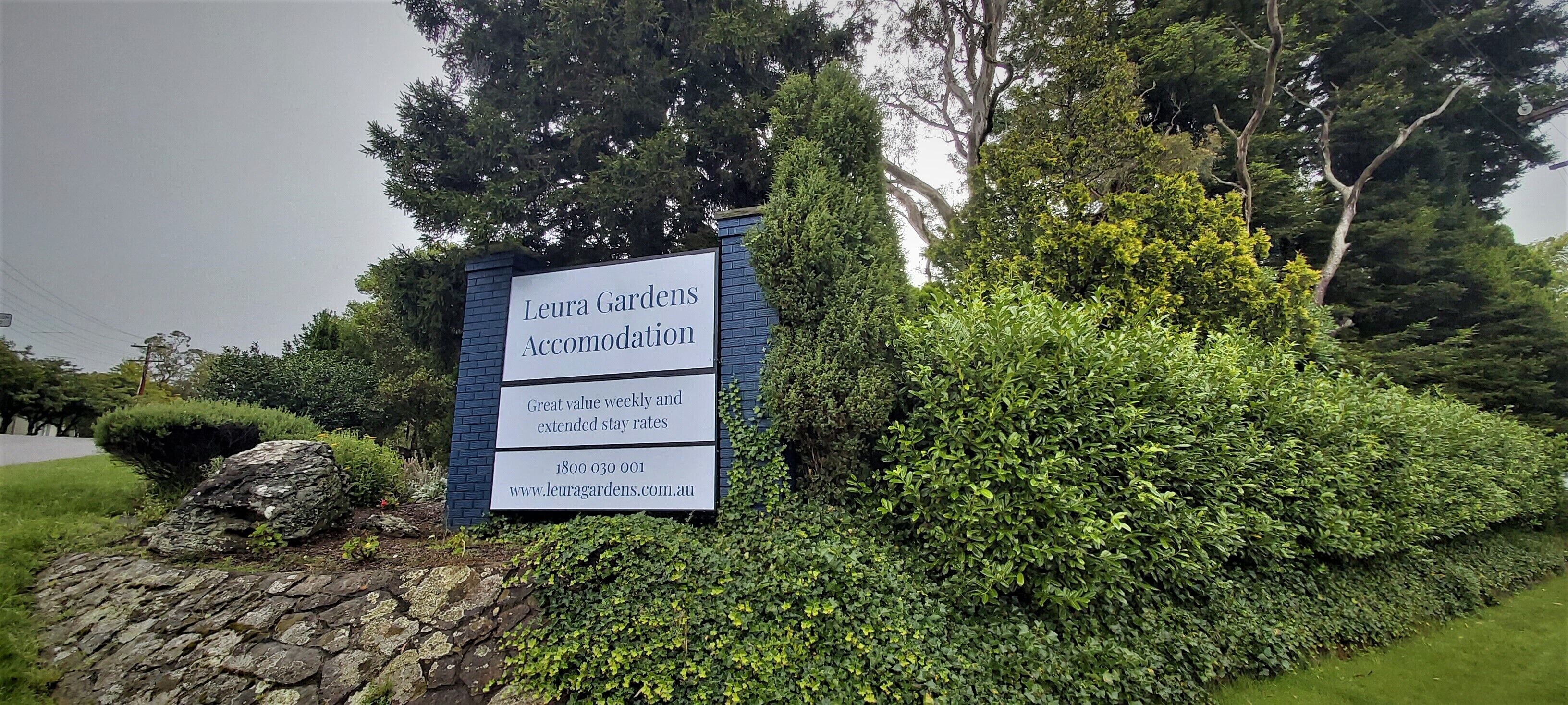 Señal de Leura Gardens Accommodation que muestra un camino de piedra y abundante vegetación.