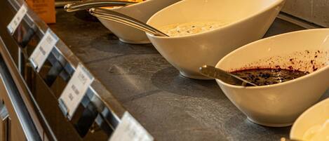 Un buffet proposant différents plats, notamment des fruits et un plat contenant une sauce foncée.