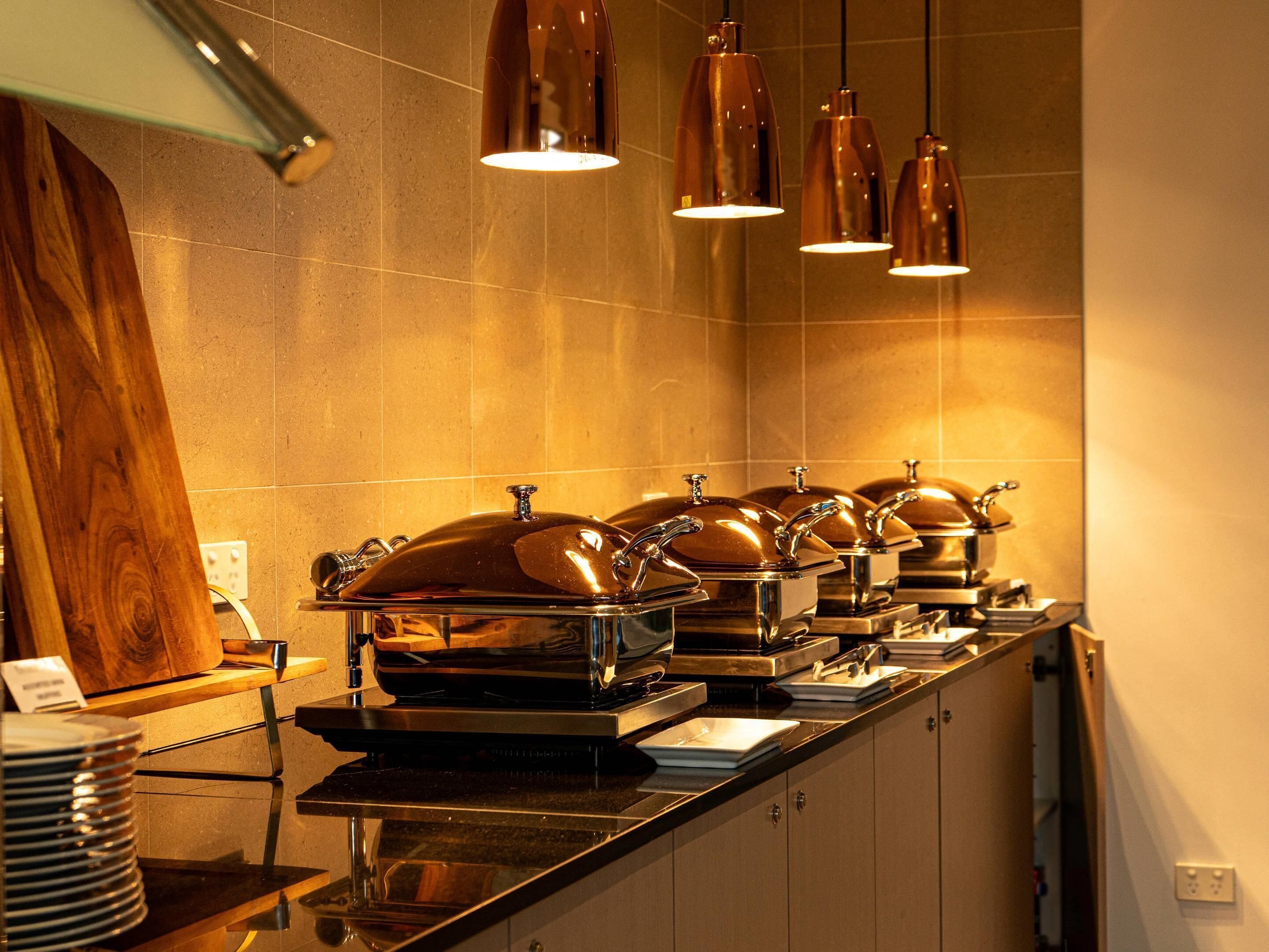 A buffet setup with multiple food service stations, each with a covered serving dish and a metal tray.