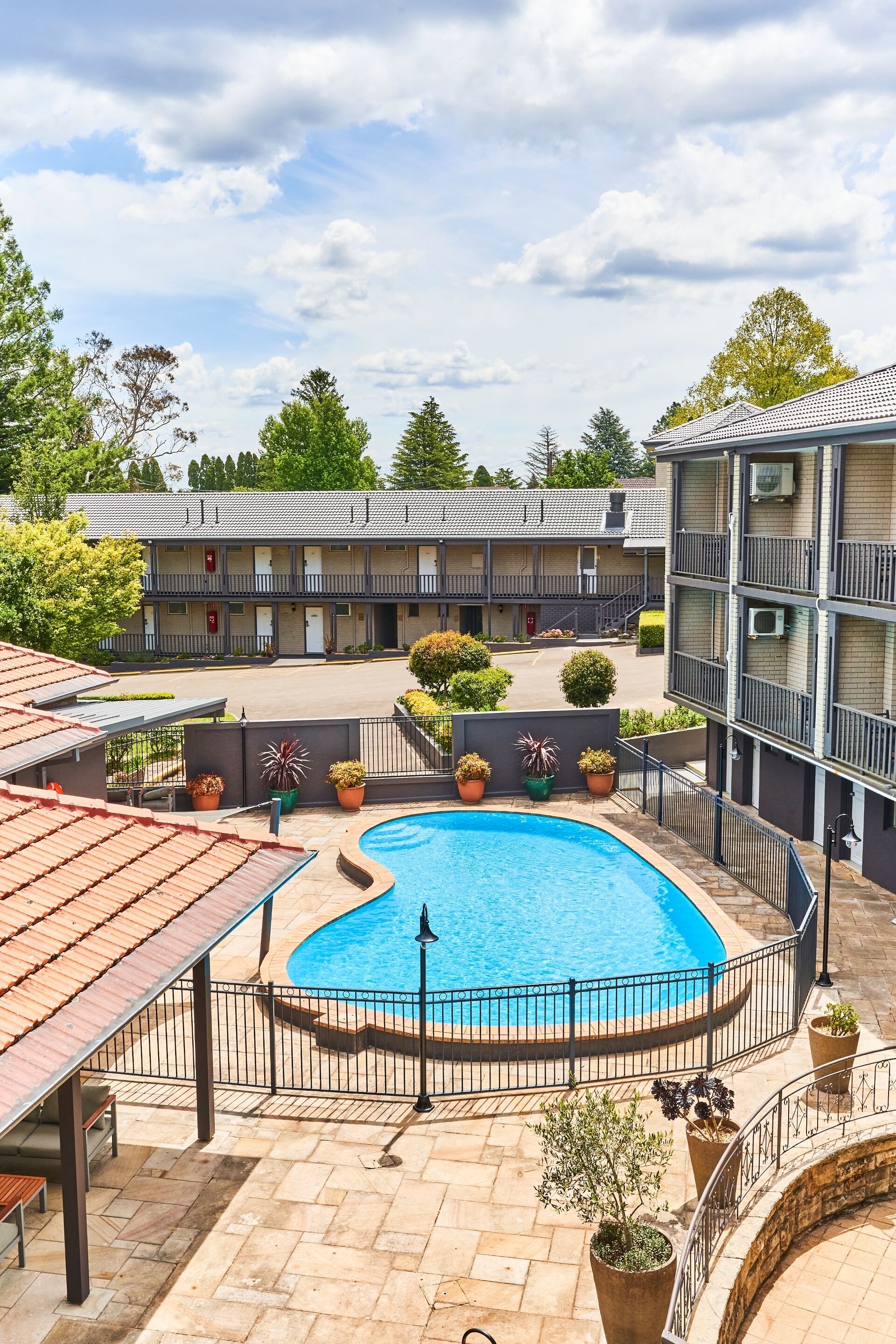 A hotel with a swimming pool, outdoor seating, and a parking area.