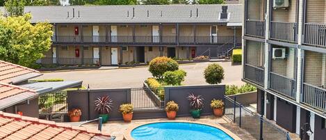 A hotel with a swimming pool, outdoor seating, and a parking area.