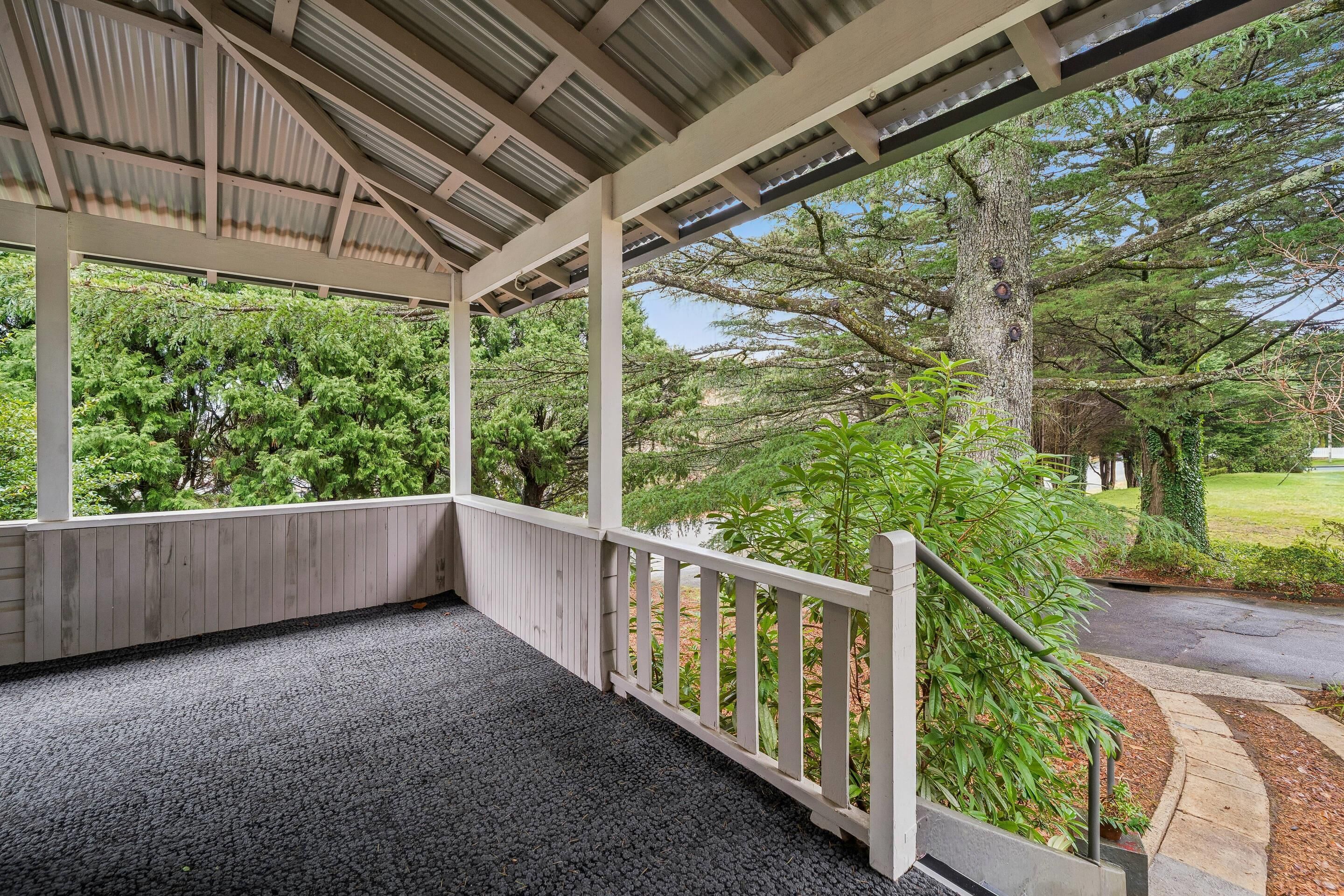 A covered porch with a view of a landscaped garden and trees.