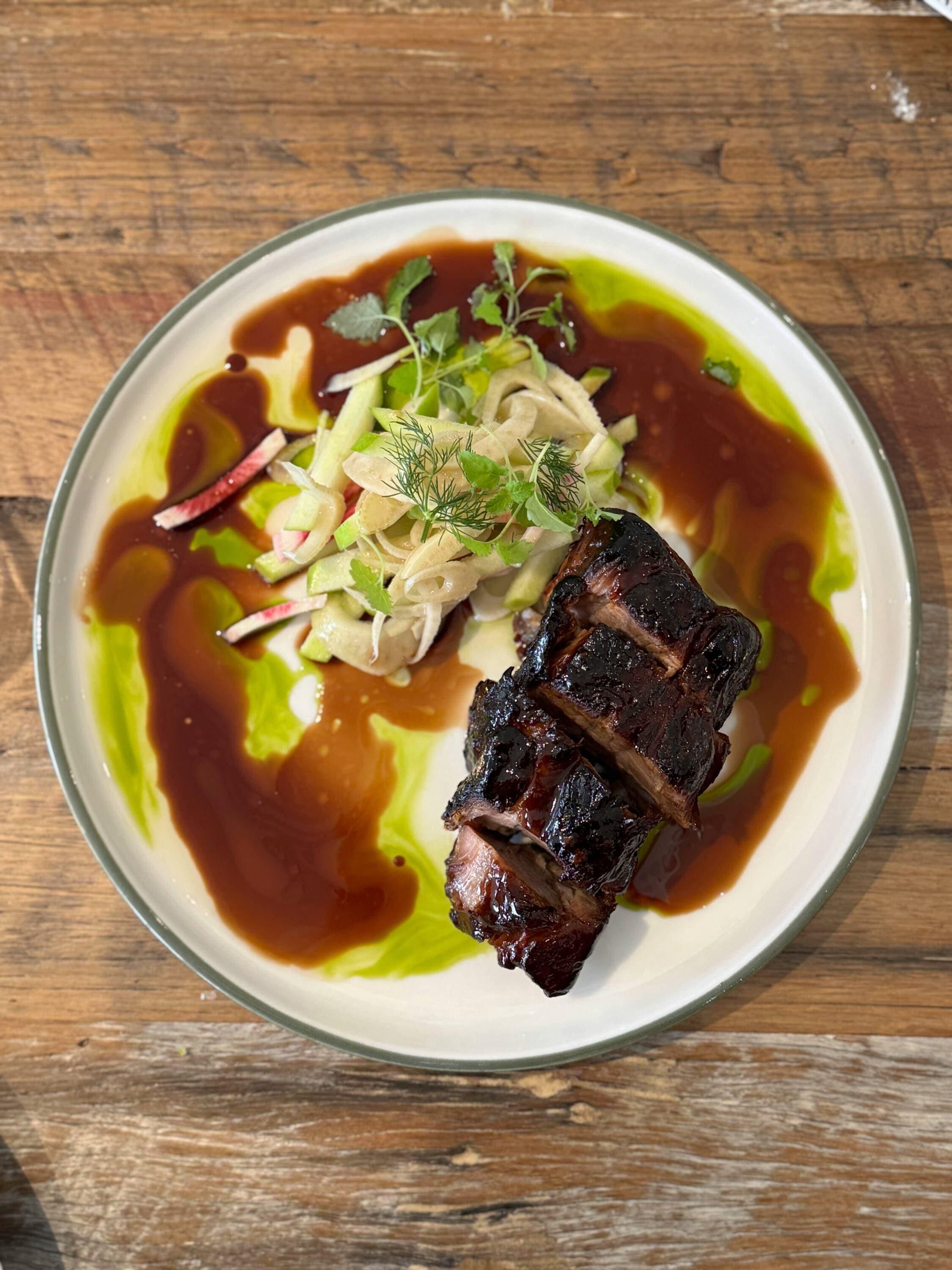 Un plato con un trozo de carne, salsa verde y una ensalada.