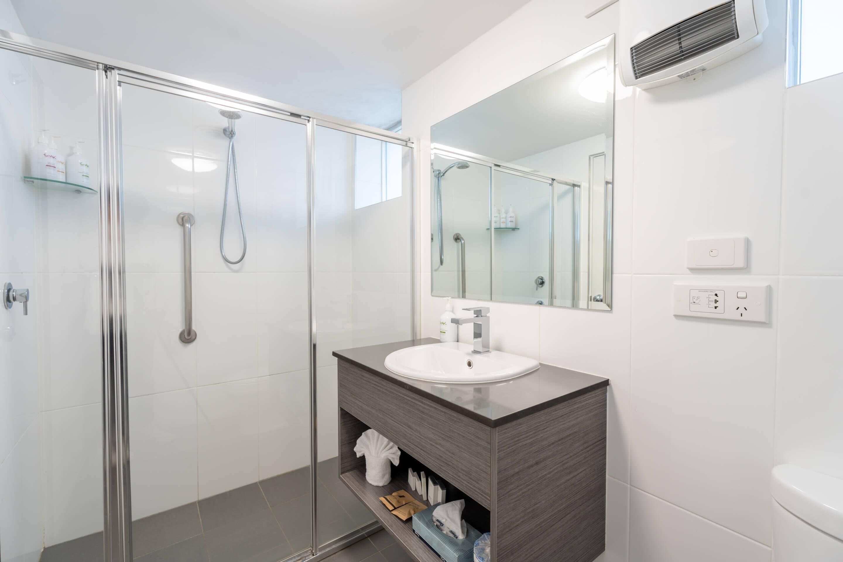 A modern bathroom with a glass shower enclosure, a white sink, and a mirror above it.