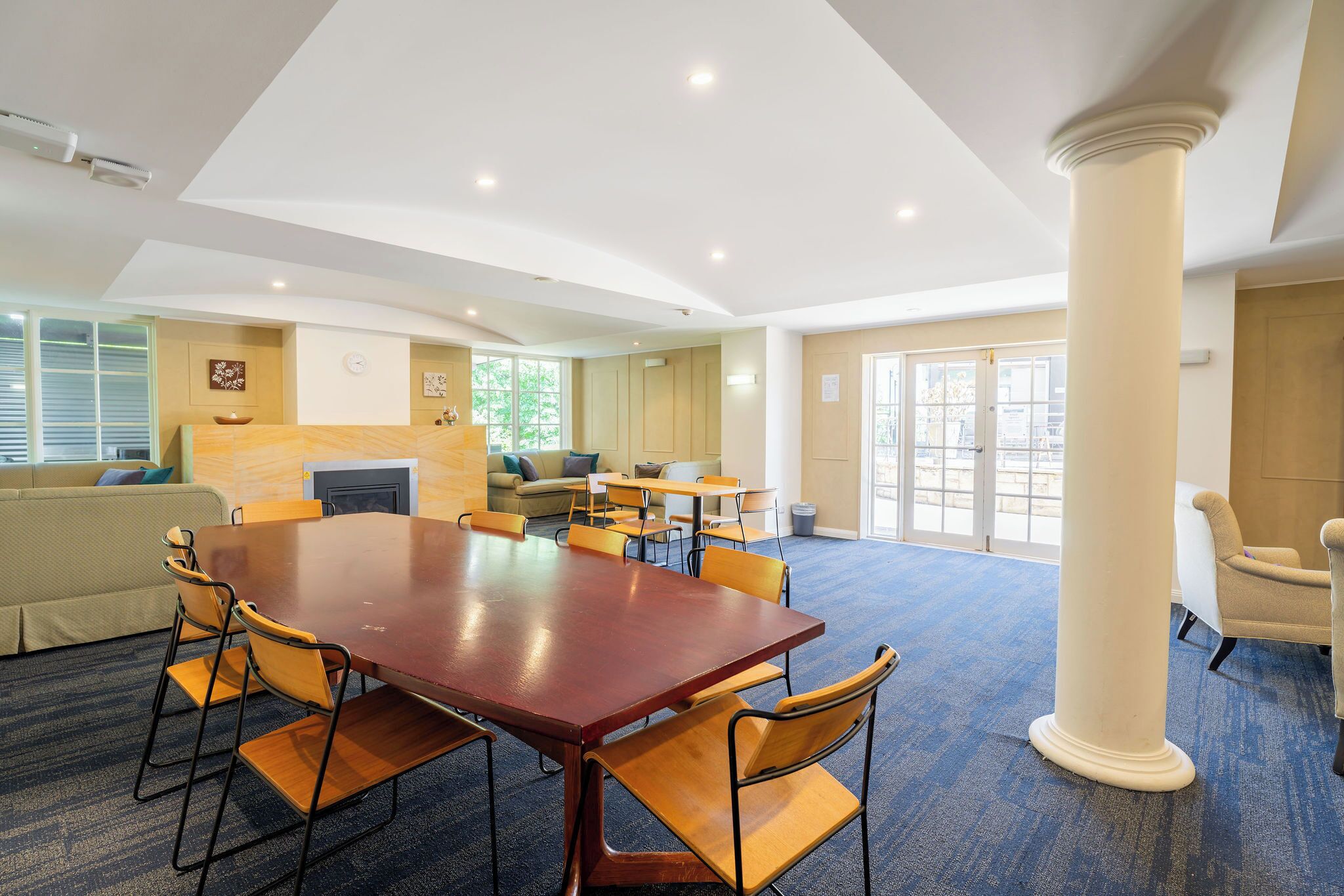 A conference room with a large wooden table, multiple chairs, a sofa, and a large pillar.