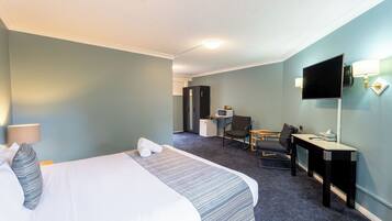 A hotel room with a bed, a desk, a chair, a TV, and a desk lamp.