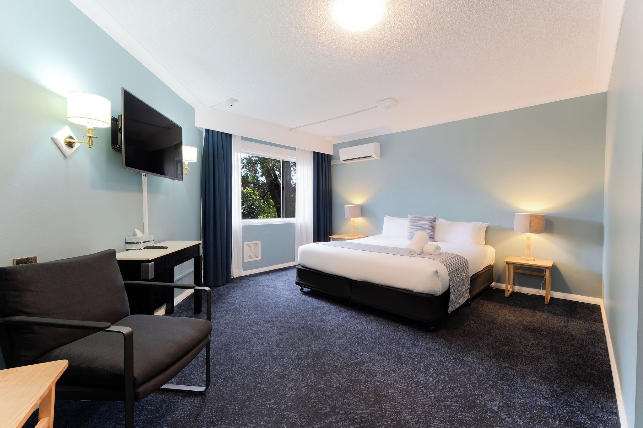 A hotel room with a bed, a desk, a chair, a TV, and a window with curtains.