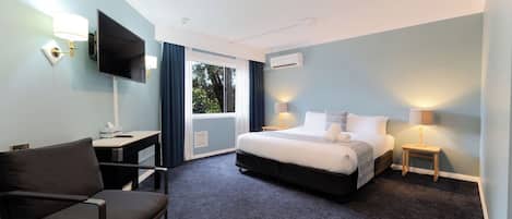 A hotel room with a bed, a desk, a chair, a TV, and a window with curtains.