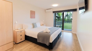 Een moderne slaapkamer met een bed, nachtkastjes, een kledingkast en een schuifglazen deur die leidt naar een balkon.
