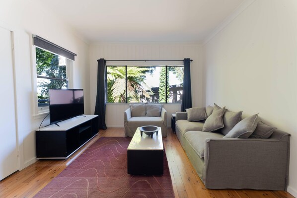 Una sala de estar con televisión, sofá, mesa de centro y ventanas amplias.