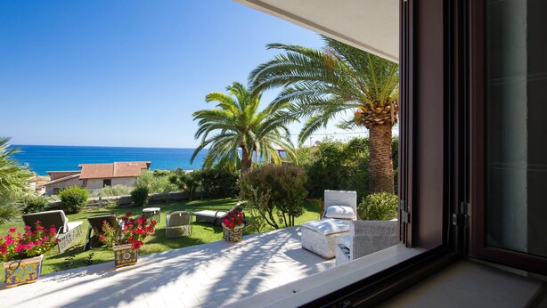 Ein Balkon mit Meerblick, Gartenmöbel und ein Garten mit Palmen.