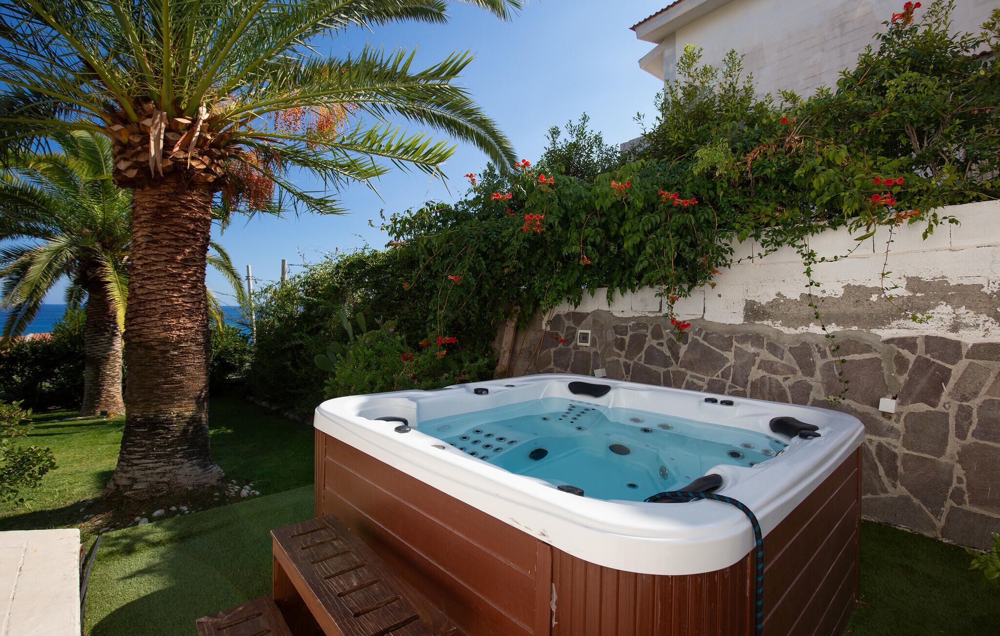 A hot tub in a garden with a palm tree and flowering plants.