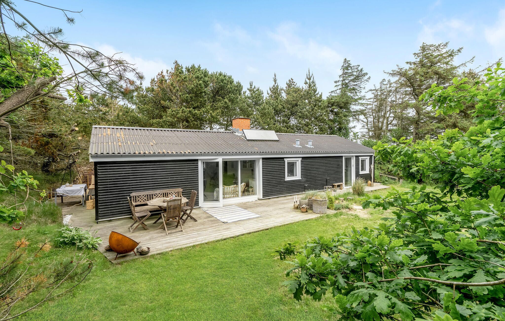 A compact, single-story cabin with a dark exterior, a small deck, and a patio area.
