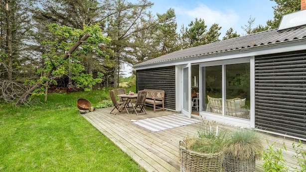 A modern house with a deck, outdoor furniture, and a fire pit.
