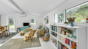 A spacious room with a large bookshelf, a comfortable seating area with a sofa and chairs, a television, and a view of the outdoors through large windows.