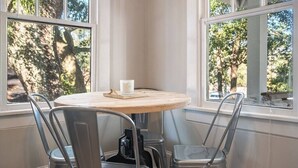 Une table ronde avec un plateau en bois et des chaises en métal, placée près des fenêtres, d’où l’on peut admirer les arbres.