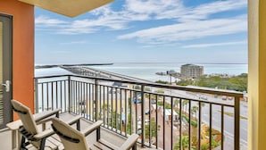 Un balcon avec deux chaises et une table, offrant une vue sur la côte, avec un pont, une route et des bâtiments.