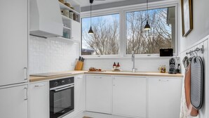 Eine moderne Küche mit weißen Schränken, einem eingebauten Ofen, einer Holz Arbeitsplatte und einem Fenster mit Blick auf kahle Bäume.