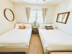 Una habitación con dos camas, una ventana con cortinas, una lámpara y un espejo en la pared.
