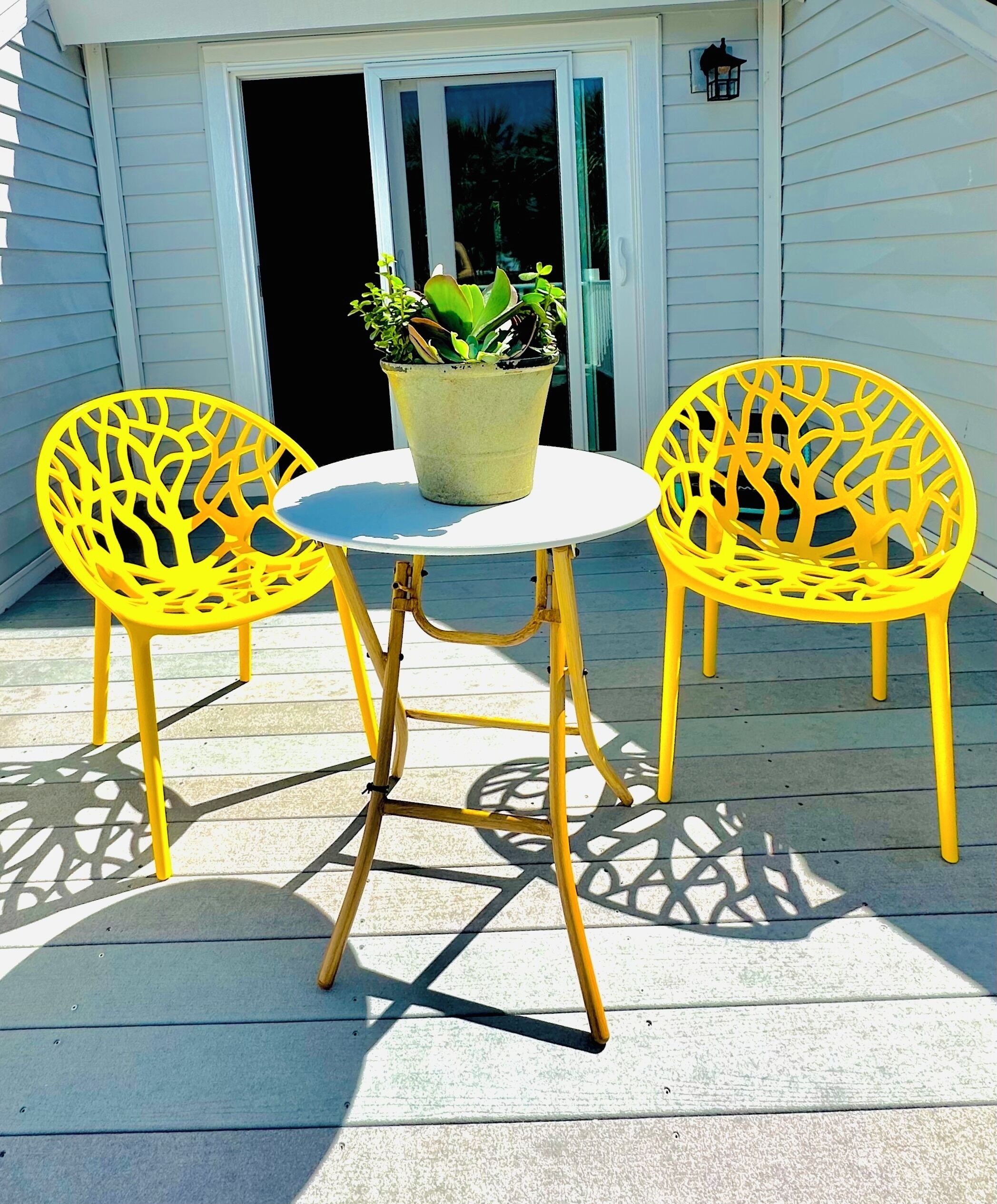 Eine Terrasse mit zwei gelben Stühlen und einem Tisch, einem Blumentopf und einer Tür mit Fenster.