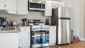 Une cuisine moderne avec des armoires blanches, des appareils en acier inoxydable, notamment un four à micro-ondes, un four et un réfrigérateur, et un comptoir en granit.