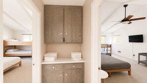 Una camera da letto con un letto a castello, una scrivania con una sedia, una ventola a soffitto e una TV appesa al muro.