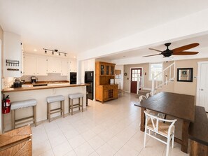 Een ruime keuken met een centraal eiland, houten kastjes en een eetgedeelte met een grote tafel en stoelen.