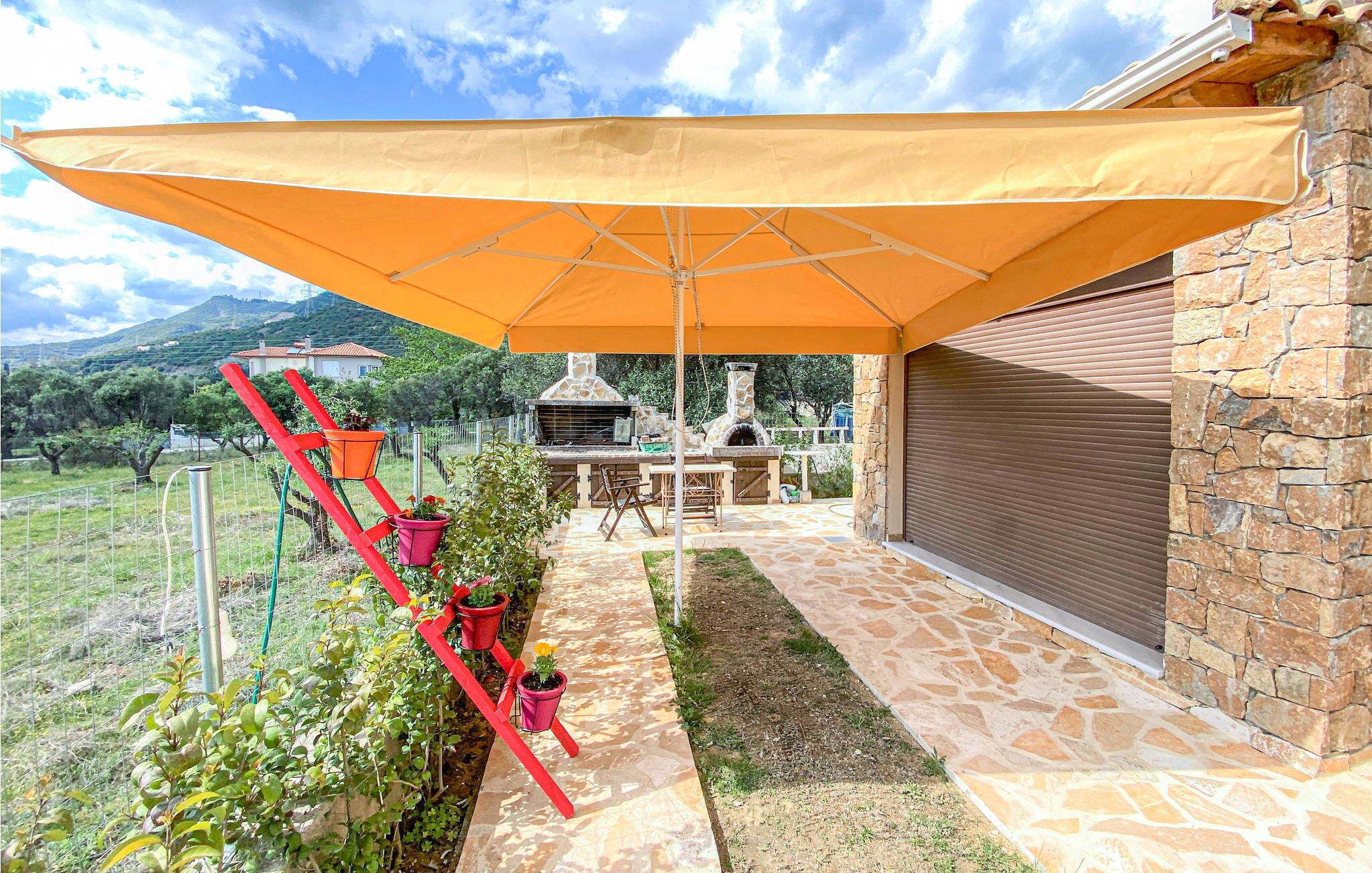 An outdoor patio with a stone floor, a brick wall, and a large orange canopy.