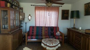 A living room with a sofa, a wooden cabinet, a ceiling fan, and a patterned rug. - Wild Creek BnB, " Cottage " (Dyer)