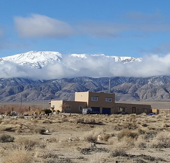 A two-story building with a flat roof, surrounded by a dry, grassy landscape with mountains in the background.