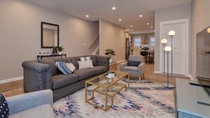 A modern living room with a grey sofa, a glass coffee table, and a patterned rug.